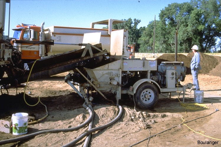 A grout pump with lines running to grout pipes. The silty sand material used in grout mix can be seen in the background.<br />(Courtesy of Dr. Ross Boulanger, UC Davis). A grout pump with lines running to grout pipes. The silty sand material used in grout mix can be seen in the background.<br />(Courtesy of Dr. Ross Boulanger, UC Davis).
