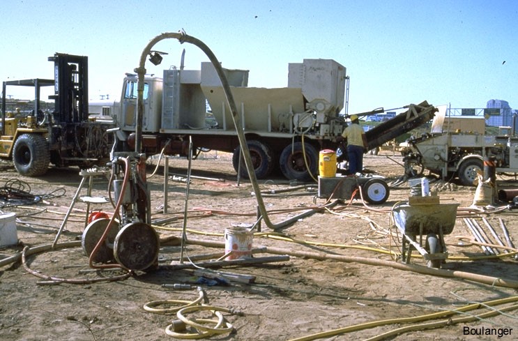 Grout lines run from the pump to the casing installed in the ground. The casing is held in place by a hydraulic jack.<br />(Courtesy of Dr. Ross Boulanger, UC Davis). Grout lines run from the pump to the casing installed in the ground. The casing is held in place by a hydraulic jack.<br />(Courtesy of Dr. Ross Boulanger, UC Davis).
