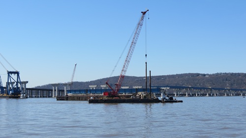 Crane on platform lifting piles out of the water.
